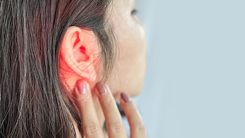 Woman touching a painful ear that is glowing red