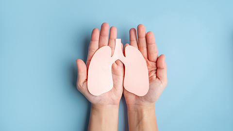 An image of hands holding a paper cutout of lungs set against a blue background.