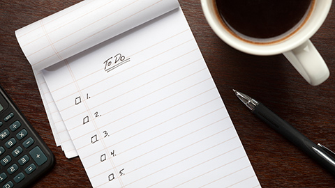 A white notebook with a to do list sitting next to a cup of coffee.