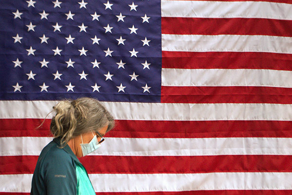 Woman wearing a face mask standing in profile in front of an American flag