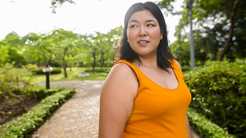 Portrait of woman wearing a yellow orange dress standing in a Bangkok park.