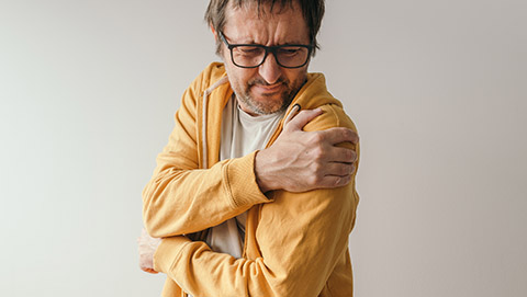 A man shown holding his left shoulder tightly in pain.