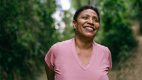 A woman smiling against a background of green trees.