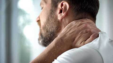 Massage client in pain rubbing his neck with his hand.