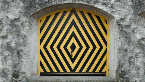 Window with black and yellow caution stripes set in a stone wall.