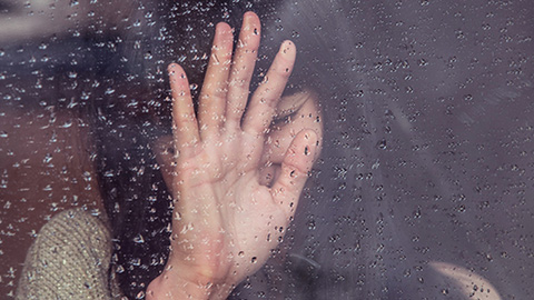 A woman's hand seen through the glass of a window through the rain