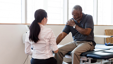 A female healthcare provider examining an older Black gentleman with shoulder pain