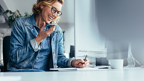 A smiling woman talking on the phone and taking notes