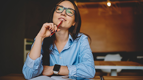 A women in glasses holding a pencil, thinking and pondering