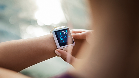 An image of a woman looking down towards her smartwatch showing her heart rate.