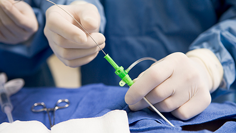 A doctor in a surgical setting placing a cardiac catheter into a patient.