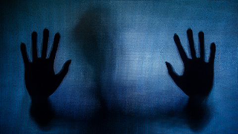 A silhouette of hands pressed against a screen against a blue background.