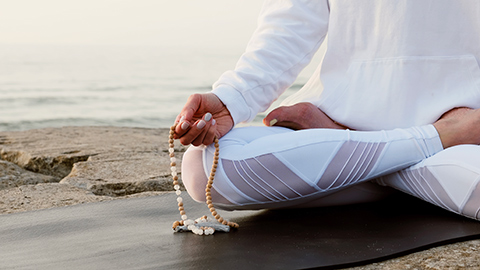 A person holding meditation beads in the yoga postion.
