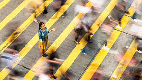 A woman stands motionless between a bustling intersection.