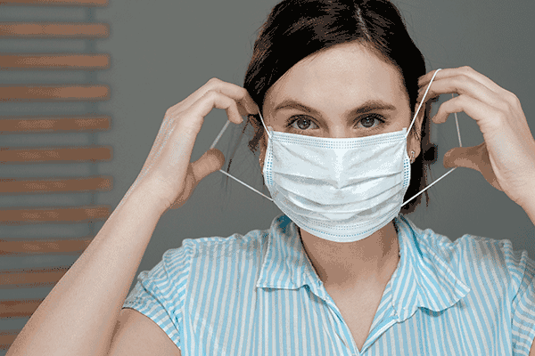 Young woman putting on a disposable surgical face mask 