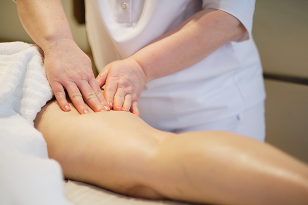Massage therapist performing manual lymph drainage massage on a client leg. 