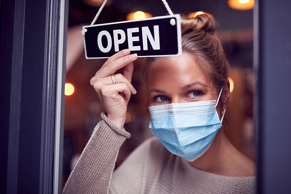 Massage therapist wearing face mask putting an Open sign on her door.