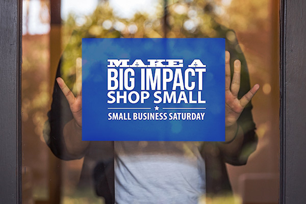 Shop owner putting up a Small Business Saturday sign on a shop window.