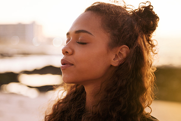 Young Black woman with her eyes closed taking a deep breath. 