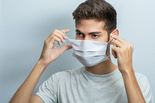 Young man raising a surgical mask to his face