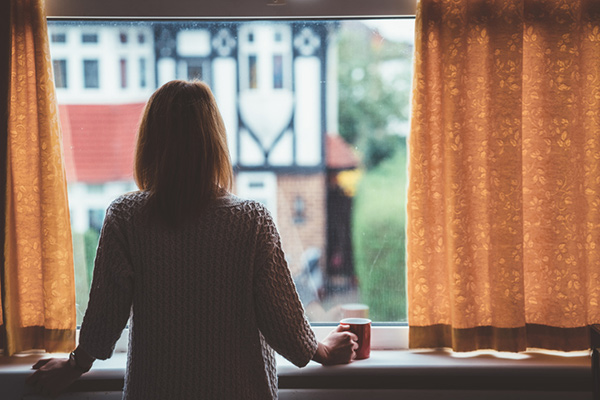 Woman with her back to the camera looking out the window with a cup of tea