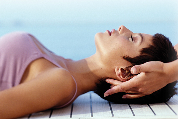 A woman lays on her back while a massage therapist performs craniosacral therapy.