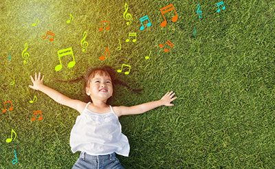 Smiling little girl lying in a field with music notes floating around her head