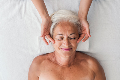 smiling senior woman receiving head massage from therapist