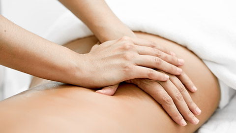 Massage therapist using both palms to massage a client’s lower back.