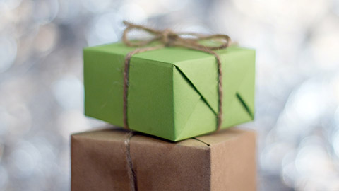 A green gift box wrapped in twine sitting atop a larger brown gift box.