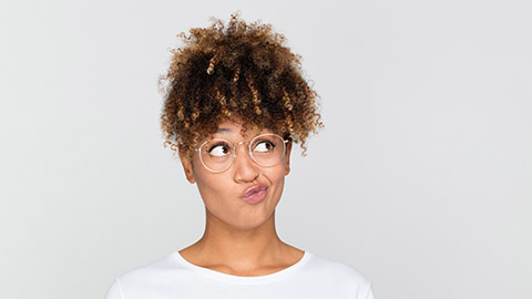 A woman with glasses stands with a curious look on her face.