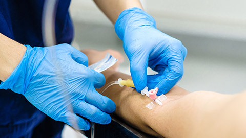 A healthcare worker shown with latex gloves drawing blood from a patients left arm.