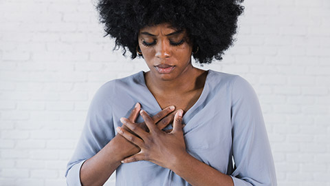 A woman hold her chest in pain with both hands clutched tightly.