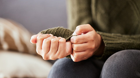 An image of a person gripping at the sleeve of their green knit sweater.