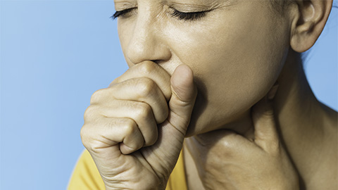 A woman holding her hand to her mouth coughing.
