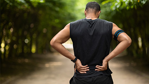Rear image of a person standing holding their lower back in pain.