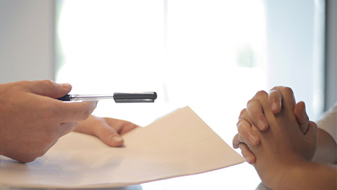Image of a hand holding a pen and paper with a client in consultation.