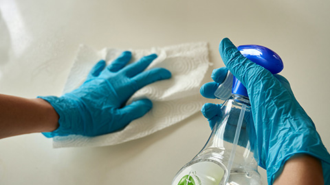 A pair of hands in gloves disinfecting a surface with a spray bottle