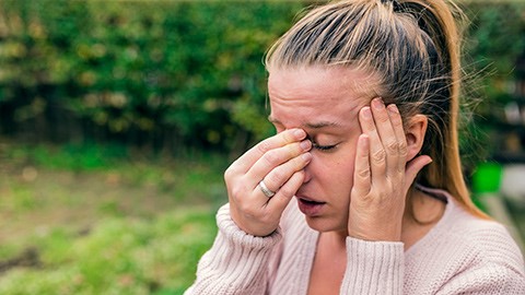 A woman with sinus pressure holds her hand to her nose and temple.