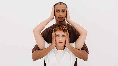 A pair of people with arms intertwined covering each other’s ears.