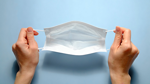 A pair of hands holding a paper surgical mask. 