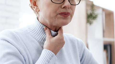 An older woman holding her throat in pain.