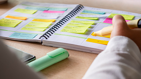 Person highlighting lines in an open schedule book with colorful post it notes.