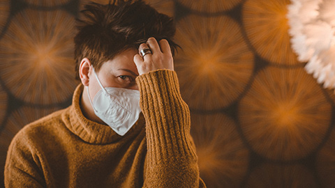 Woman wearing face mask thinking in front of backdrop of COVID virus