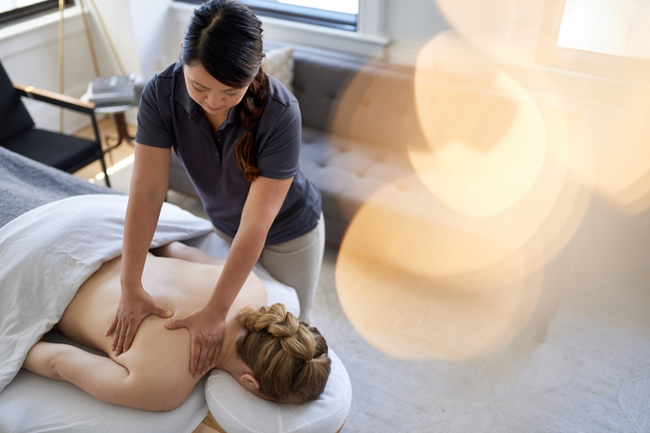 A female massage therapist treats a female client in a massage therapy studio.