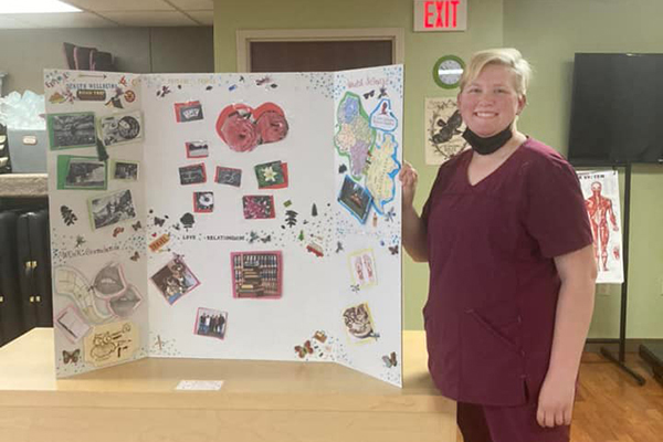 Massage Therapy student displays a trifold board in a classroom.