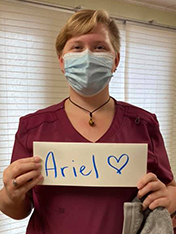 마사지 요법 학생인 Ariel Burke는 마스크를 착용하고 Ariel과 하트가 표시된 표지판을 착용하고 있습니다.