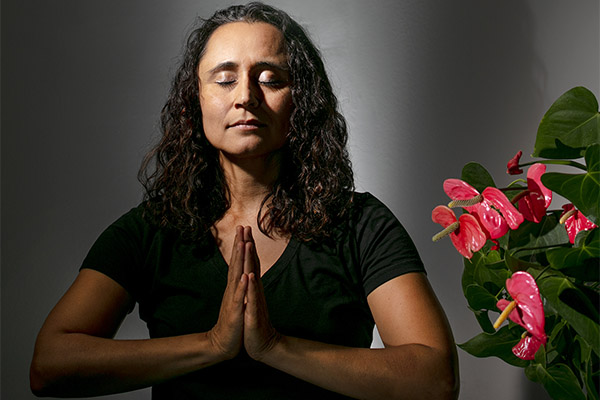 A woman, Stormy Mesa, sits and meditates next to a plant.