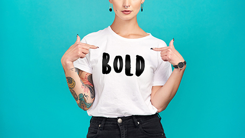 Woman with tattoos pointing to the word "Bold" on her T-shirt